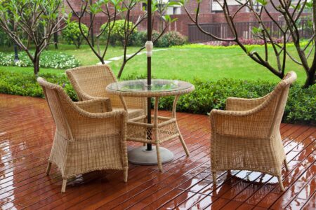 Wicker patio chairs and table near garden after raining